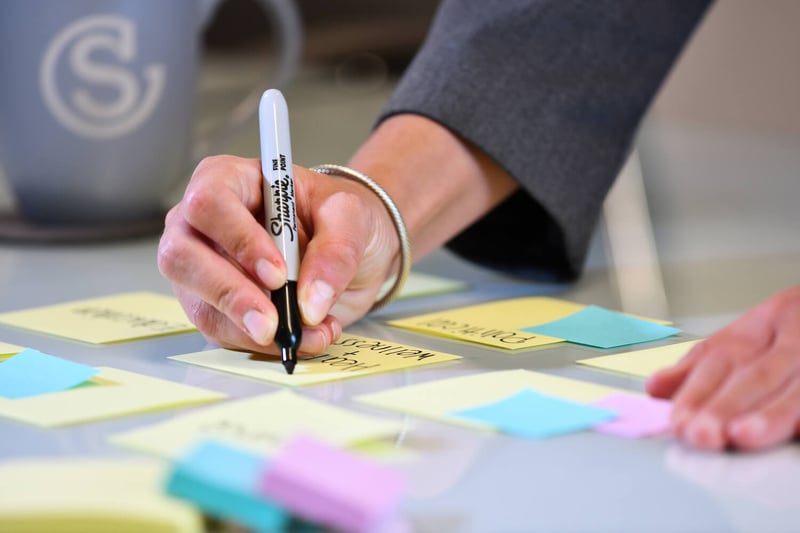 Closeup of someone using a black Sharpie marker to write on a Post-it Note