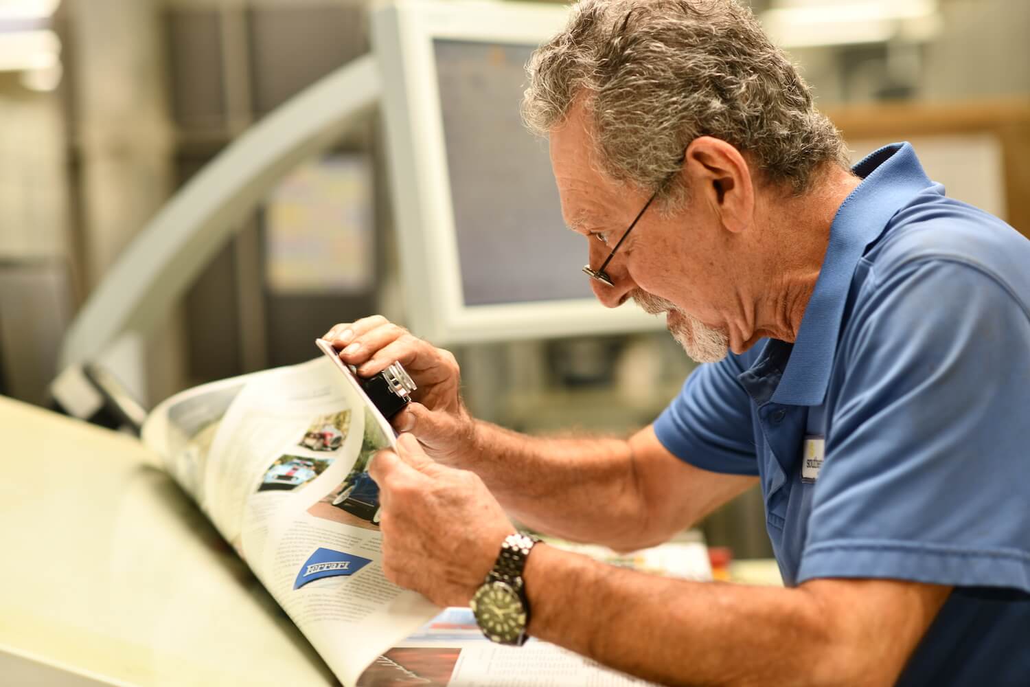 Employee examining finished print piece using a loupe magnifier