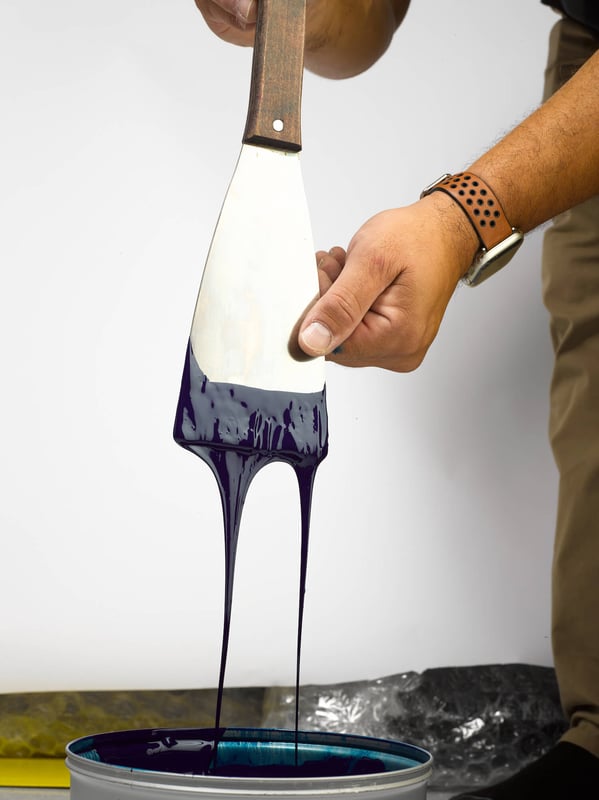 Hand holding a tool thats dripping dark blue ink into a can